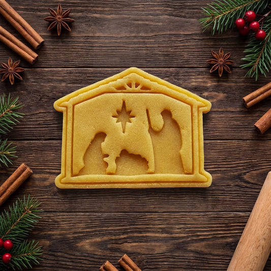 Sagoma di pasta frolla a capanna con Maria, Giuseppe, Gesù nella mangiatoia e stella, su legno tra decorazioni natalizie.
