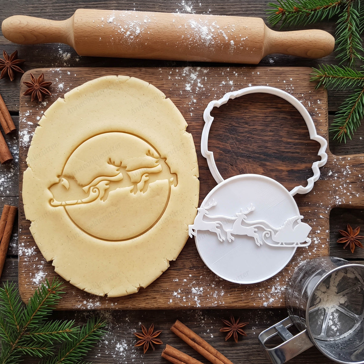 Slitta di Babbo Natale con due renne impressa nella pasta frolla, accanto alla taglierina e al timbro bianchi.
