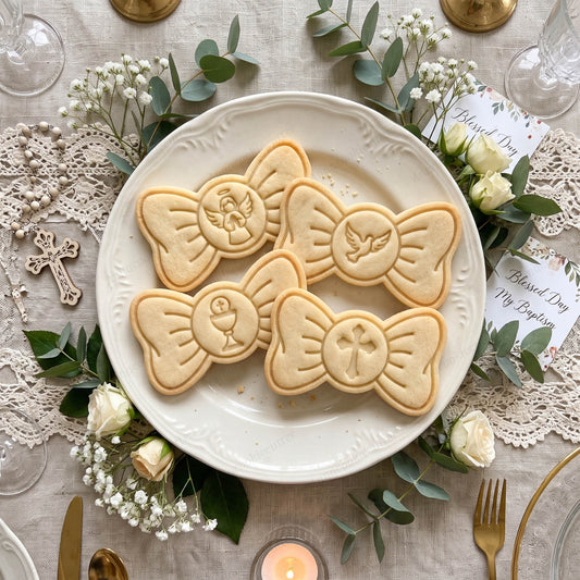 Quattro biscotti a forma di fiocco con angelo, croce, colomba e calice, su un piatto per una cerimonia.
