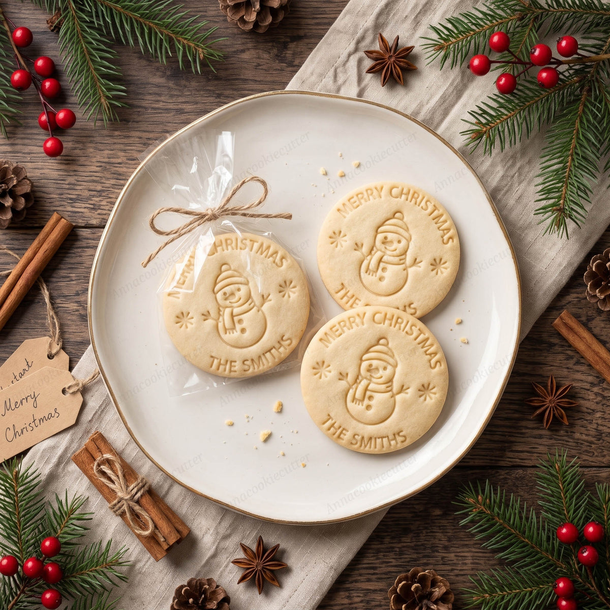 Biscotti di esempio con l'impronta del timbro del pupazzo di neve, la scritta Merry Christmas e il nome della famiglia, su un piatto bianco con decorazioni natalizie