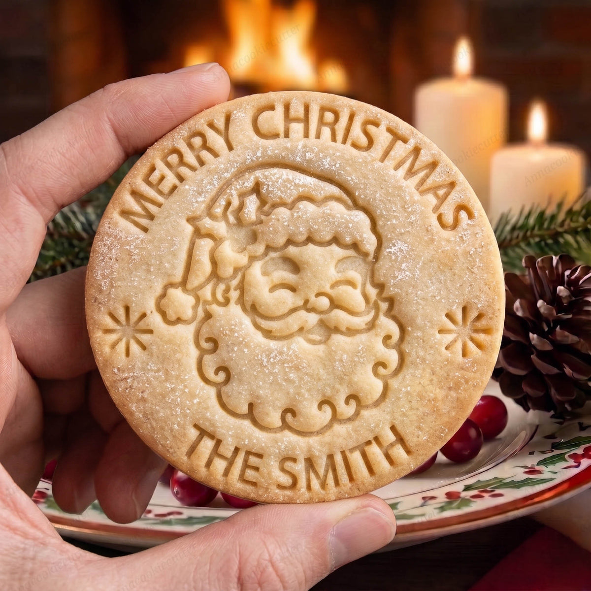 Biscotto tondo con Babbo Natale, fiocchi di neve e scritte Merry Christmas e The Smith, tenuto in mano.
